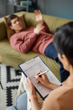 Kanepede yatıp sorunlarını anlatırken hastanın kartını dolduran psikoloğun dikey görüntüsü.