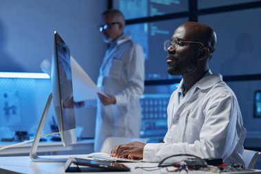 Afrika kökenli Amerikalı mühendis monitör önünde masada oturuyor ve ofiste bilgisayarla çalışıyor.