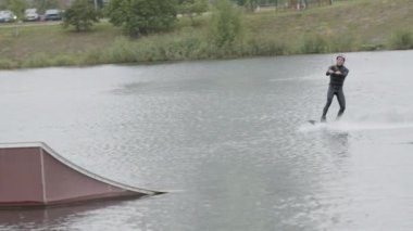 Erkek wakeboard sörfçüleri açık hava kablo parkında sürgülü kaydırak numarası yapıyor.