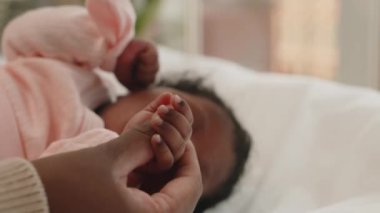 Uykulu Afrika kökenli Amerikalı bebek sırt üstü uzanıyor ve annesinin parmağını tutuyor.