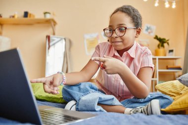 Yatakta oturan ve internetteki görüntülü konuşma sırasında dizüstü bilgisayara işaret eden tatlı liseli kız. Ya da uzaktan eğitim alırken.