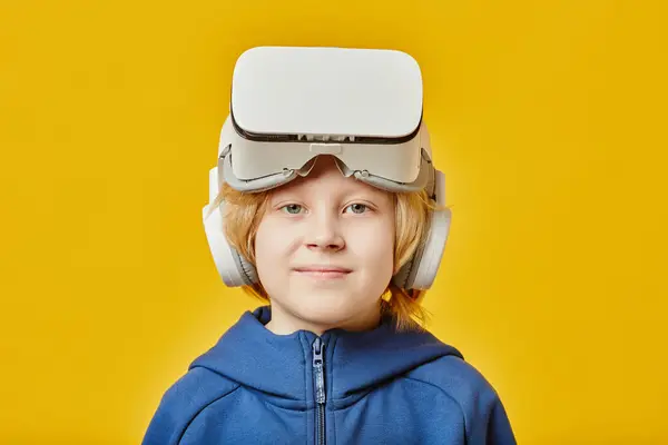 stock image Cute blond boy with VR headset on forehead looking at camera after playing virtual game while standing over yellow background