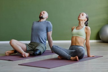 Özürlü bir adamla birlikte yoga terapisi yapan ve gözleri kapalı meditasyon yapan genç bir çift.