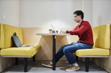 Gözlüklü genç Arap adamın tam boy yan görünüm portresi ve elektrikli ışıklandırma kabininde dizüstü bilgisayar kullanımı, kopyalama alanı