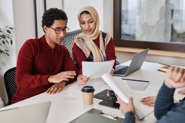 Bir grup modern Arap iş adamı toplantı masasında birlikte çalışıyor ve belgeleri ellerinde tutuyorlar.