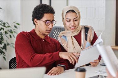 İki modern Arap iş adamı ve kadın toplantı masasında birlikte çalışıyor ve belgeleri tartışıyorlar.