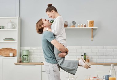 Mutfakta kucaklaşan ve eğlenen genç çiftin yan görünüm portresi.