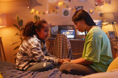 Siyahi anne ve kızının samimi kız konuşmalarının yan görüntüsü. Evde yatakta otururken.