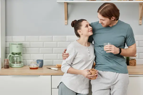 Minimal waist up portrait of affectionate young couple embracing in kitchen and looking at each other with love, copy space
