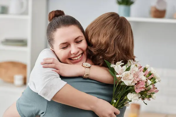 Close up of young man giving bouquet of flowers to wife and embracing in kitchen