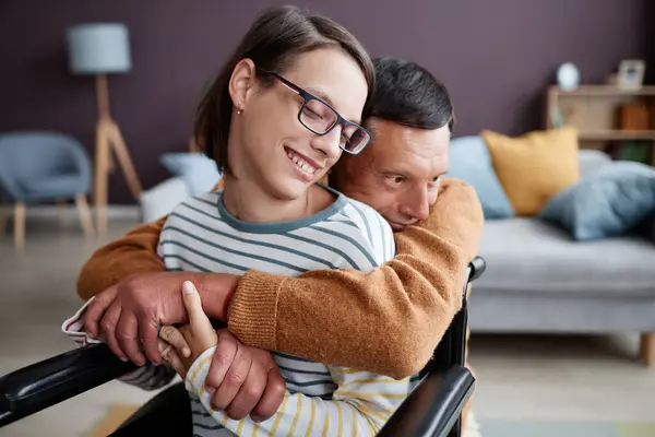 Portrait of caring father embracing smiling girl with disability at home, copy space