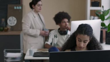 Modern bilişim ofisindeki masaüstü bilgisayarında çalışan iki farklı meslektaş arka plandaki masaüstü monitörüne bakarken, iki çift ırklı kadın programcı