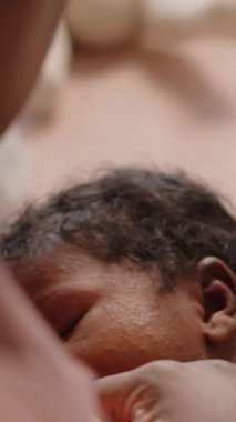 Yavru Afro-Amerikan bebeğin evde emzirildiği ve annesinin kollarında sakince yattığı dikey çekim.