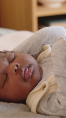 Yatakta gözleri kapalı yatan küçük Afrikalı Amerikalı bir kızın dikey çekimi. Yanında oturan bir anne tarafından öpülmek.