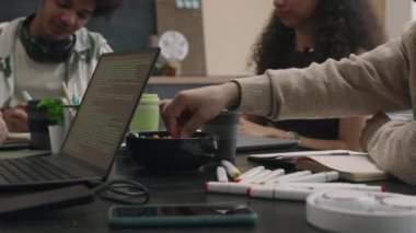 Dört kişilik yaratıcı bilişim ekibi dizüstü bilgisayar, kırtasiye ve çevre dostu kahve fincanlarıyla masada oturuyor ve ofiste yeni yazılım geliştirmeyi tartışıyorlar.