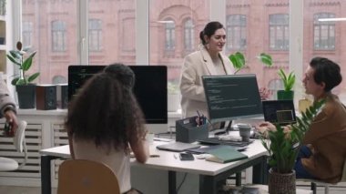 Genç erkek ve kadın programcılardan oluşan orta ölçekli bir çekim. Çağdaş bilişim ofisinde büyük pencereli bir çalışma günü boyunca birbirleriyle etkileşim halindeler.
