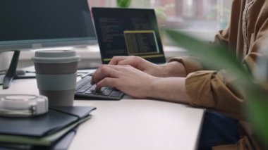 Modern bilişim ofisinde masa başında oturan kablosuz klavyeye program kodları yazan tanınamayan bir erkek programcının görüntüsü.