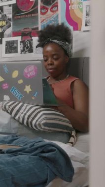 Kucağında dizüstü bilgisayarı olan, hafta sonu evden ders çalışan Afrikalı Amerikalı bir kadının dikey görüntüsü.