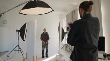 Profesyonel erkek fotoğrafçının video kamera ile fotoğraf çektiği arka plan görüntüsü ve kapalı alanda asistan olarak çalışırken bilgisayar monitöründeki resimlere bakması.