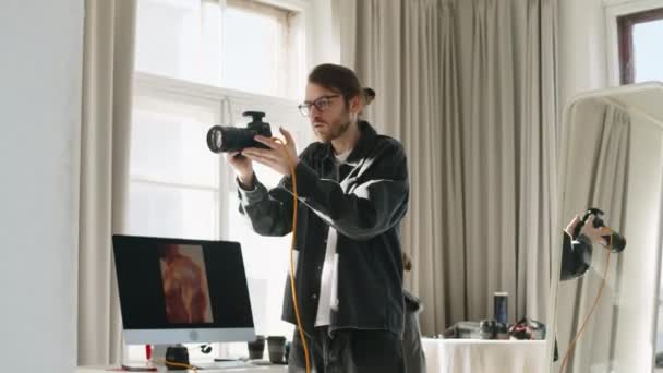 Dslrカメラを使用してアシスタントと若い写真家のミディアムショットは 写真撮影中に明確なスタジオ背景にポーズするシャツレスの男性ボディビルダーと作業しながら — ストック動画