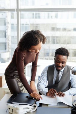 Profesyonel siyahi bir adamın patron olarak dikey portresi ve asistanı özel ofiste evrak imzalıyor.