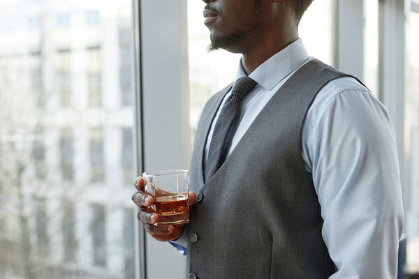 Крупный план успешного черного бизнесмена, наслаждающегося стаканом виски за окном в офисе, копировальное пространство