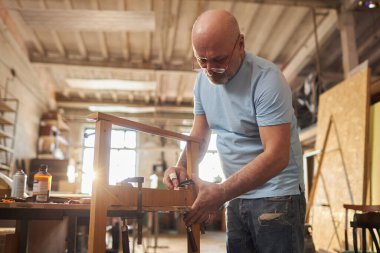 Tecrübeli kıdemli zanaatkârın marangozluk atölyesinde ahşap mobilyalar yapan düşük açılı portresi.