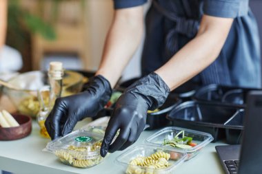 Yemek siparişlerini plastik kaplara koyarken eldiven takan kadın kafe çalışanlarını kapatın. Boşlukları kopyalayın.