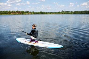 Özürlü bir gencin portresi gölde sörf yaparken spor malzemeleriyle eğleniyor.