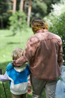 Baba ve oğlunun çöpleri toplarken parkta kucaklaşmalarının arka plan görüntüsü.