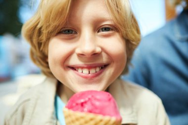 Karnavalda dondurma yiyen ve kameraya gülümseyen mutlu çocuğa yaklaş.