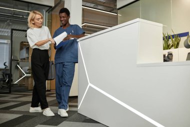 Üniformalı genç, kendine güvenen erkek klinisyen. İkisi de resepsiyonda beklerken sarışın kadın puanlarını açıklıyor.