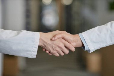 Laboratuvar önlüklü iki klinisyenin elleri kameranın önünde beklerken birbirini selamlıyor ya da hastanede tebrik ediyor.