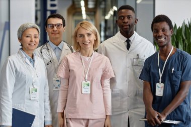 Hastane koridorunda kameranın önünde duran ve iş toplantısında gülümseyen beş mutlu genç ve deneyimli doktor.