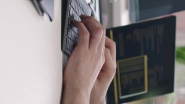 Modern bilişim ofisindeki masasında oturan kablosuz klavyede tanımlanamayan erkek programcının dikey kırpılmış görüntüsü.