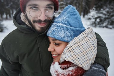 Kışın ormanda sarılıp eğlenen mutlu genç çiftin yakın plan portresi.