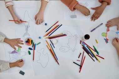 Çok ırklı çocukların sanat ve zanaat yaptığı ana okulundaki masada deniz canlılarını renklendirdiği yakın çekim.