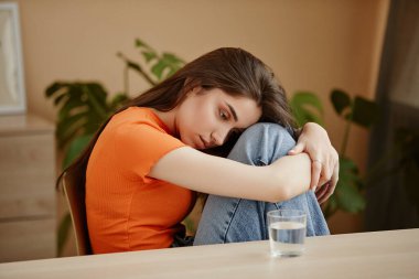 Sandalyeye kıvrılmış, zihinsel sorunları olan depresif genç kadın portresi.