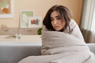 Evdeki battaniyelere sarılı, depresyonla boğuşan, fotokopi çeken üzgün genç kadın portresi.