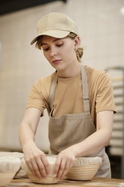 Fırın mutfağında çalışırken taze hamuru kaselere koyan genç kadının dikey portresi