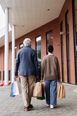 Alışveriş torbalarıyla alışveriş merkezlerinin etrafında dolaşan son sınıf çifti.