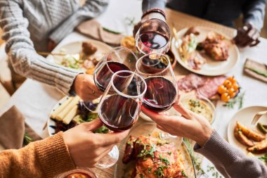 Close up of group of friends toasting with red wine glasses at festive dinner table, copy space clipart