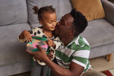 Mutlu bir siyah babanın portresi evde küçük şirin bir kıza hediyesini veriyor ve onu yanağından öpüyor.