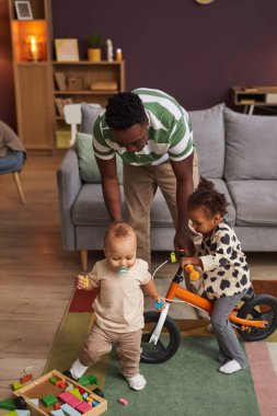 İki küçük çocukla oynayan mutlu siyah babanın dikey portresi.