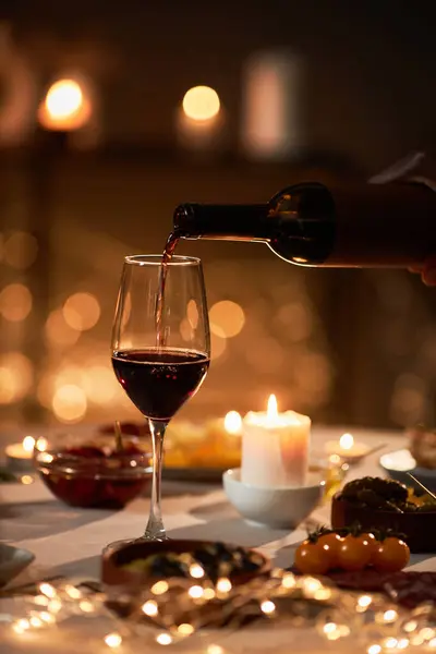 Close up of red wine pouring into glass at festive dinner table with Christmas lights in background
