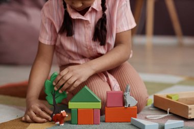 Kapatın küçük kız tahta oyuncaklarla oynayın ve evdeki yumuşak halıda otururken oyuncak ev yapın, boşluğu kopyalayın.