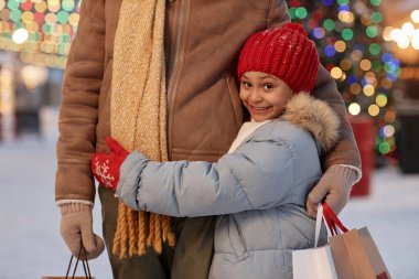 Kışın babasını kucaklayan ve elinde alışveriş torbalarıyla gezen sevimli siyah kız.