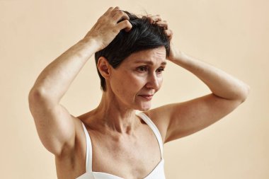 Olgun bir kadının, kafa ve kafa derisini kaşıyan, cilt hastalığından muzdarip minimum portresi.