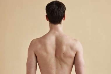 Bej arka planda çıplak duran, tanınmayan genç adamın arka görüntüsü, boşluğu kopyala