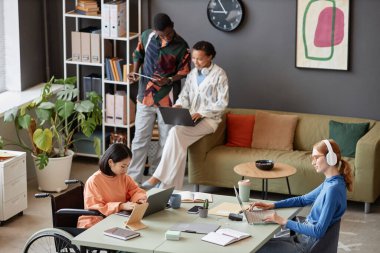 Ortak masada çalışan modern profesyonellerden oluşan çeşitli takımlarla çalışan iki genç kadının yan görünüm portresi.